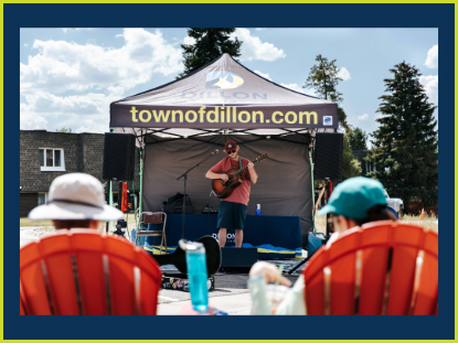 A musician playing guitar near a tent, surrounded by nature, evoking a sense of relaxation and enjoyment.