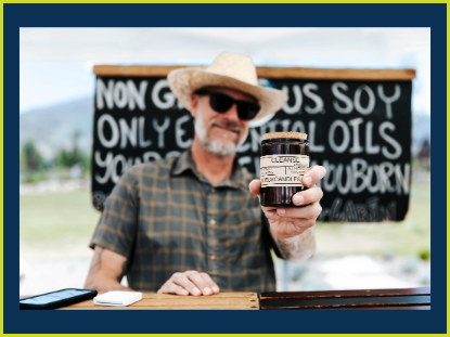 A man wearing a straw hat smiles while holding a candle in his hands, showcasing a rustic, sunny atmosphere.