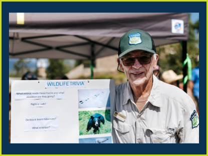 A man wearing a hat and glasses is holding a poster, smiling confidently at the camera.