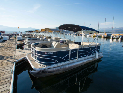 A pontoon boat is securely docked at a wooden dock, surrounded by calm water and greenery.