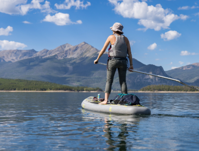 A woman paddles on an inflatable paddle board in calm waters, enjoying a sunny day outdoors.