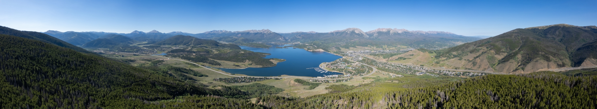 Panoramic view of a serene lake surrounded by majestic mountains under a clear blue sky.