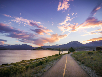 A scenic road leads to a tranquil lake, framed by majestic mountains in the background