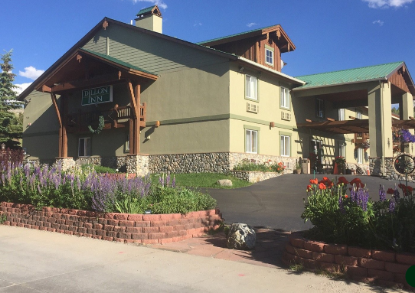 Exterior of the Dillon Inn, a green-roofed hotel with landscaped flower beds and a covered entrance on a sunny day.