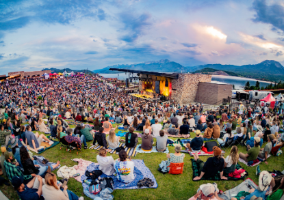 A large crowd of people enjoying an outdoor concert, sitting on the grass under a clear sky.