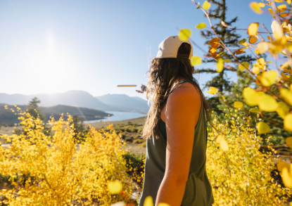 A woman wearing a hat and white shirt gazes at the mountains in the distance, enjoying the scenic view.