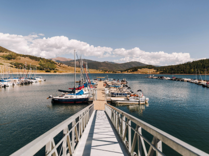 A serene lake dock with several boats moored, surrounded by calm waters and lush greenery.